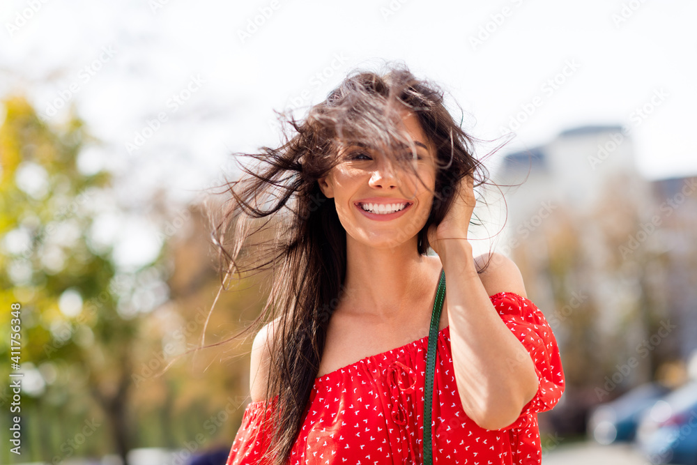 Photo portrait of smiling cheerful woman going on summer town streets in sunny windy weather in red clothes