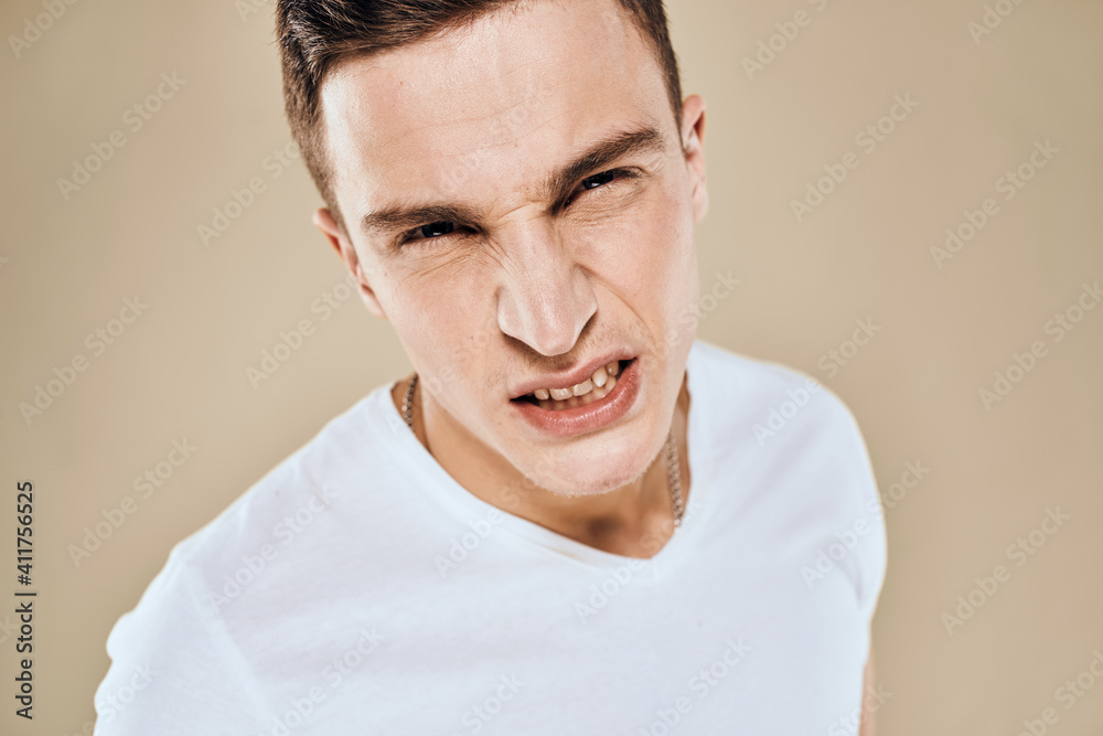 Man with displeased facial expression emotions white t-shirt gestures with hands beige background Man with displeased facial expression emotions white t-shirt gestures with hands beige background