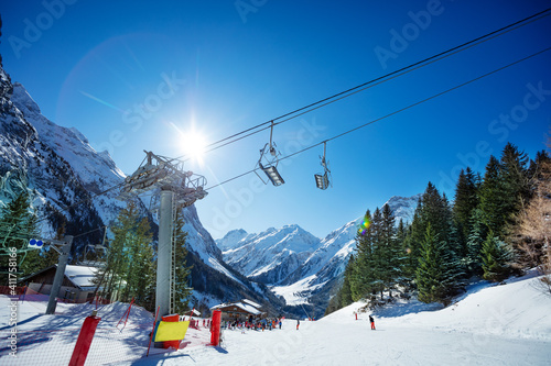 Mountain skiing trail on the sunny day in sunlit with French Alps mountains, ski lift and chairs on foreground photo