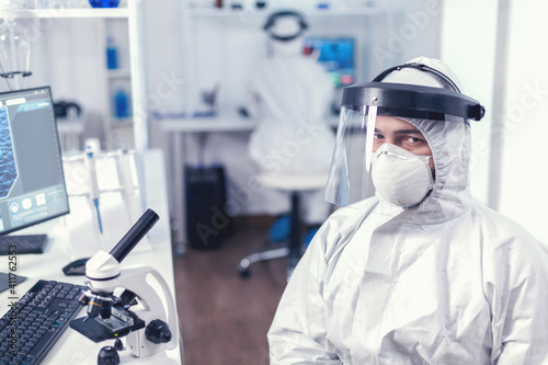 Tired chemical engineer in protection suit against infection with covid19 looking at camera.Overworked researcher dressed in protective suit against invection with coronavirus during global epidemic. photo
