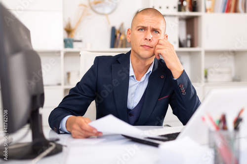 Upset man working with laptop and papers at the office