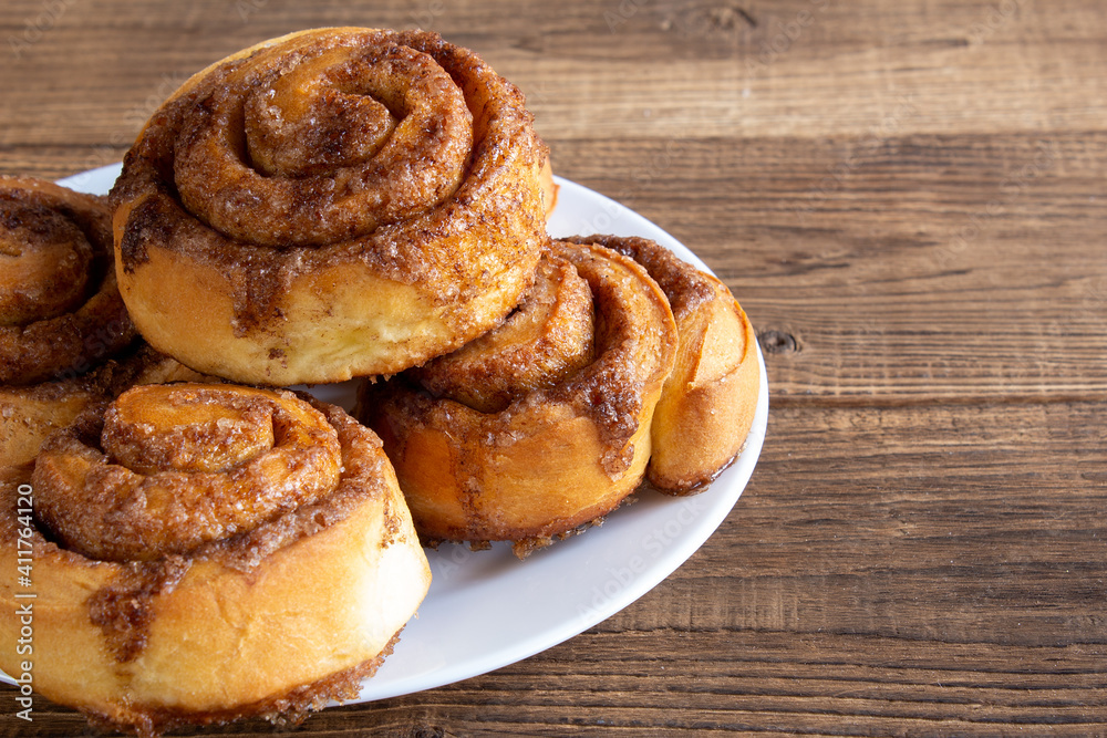 Cinnabon buns with sugar and cinnamon on a white plate on wooden background