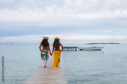 Local tahitian girls in traditional dress walking on jetty, Polynesia