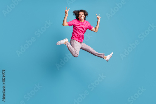 Full length body size view of attractive cheerful guy jumping running showing v-sign isolated over bright blue color background