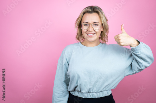 Young caucasian woman wearing sweatshirt over pink background success sign doing positive gesture with hand  thumb up smiling and happy. cheerful expression and winner gesture.