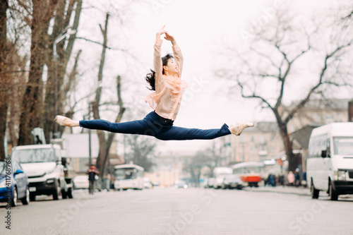 Japanese ballerina performs split and jumps in the city street.