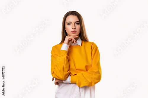 Pensive brunette girl with thoughtful expression, keeps hand on chin, plans something or makes choice, white background