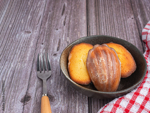 Madeleine homemade traditional French small cookies on black a dish with a cloth placed on a wooden background. Lemon glaze madeleines. Seashell sweet cakes photo