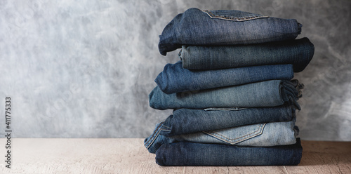 Stack of folded jeans on gray background. Copy space.