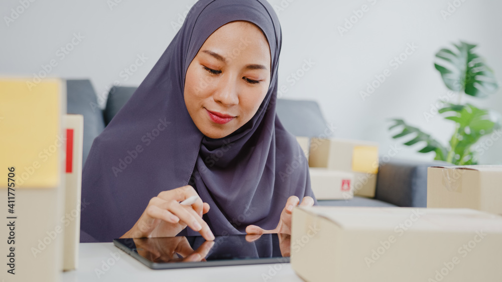 Young Asia muslim businesswoman check product purchase order on stock and save to tablet computer work at home office. Small business owner, online market delivery, lifestyle freelance concept. Young Asia muslim businesswoman check product purchase order on stock and save to tablet computer work at home office. Small business owner, online market delivery, lifestyle freelance concept.