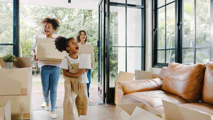 Happy African American young family bought new house. Mom, Dad, and child smiling happy hold cardboard boxes for move object walking into big modern home. New real estate dwelling, loan and mortgage.