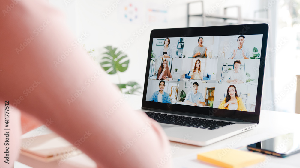 Fototapeta premium Young Asia businesswoman using laptop talk to colleague about plan in video call meeting while work from home at living room. Self-isolation, social distancing, quarantine for corona virus prevention.