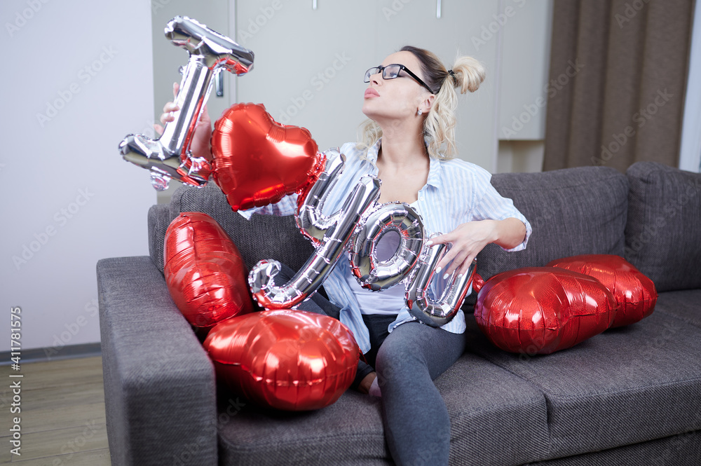 A young beautiful woman is sitting on a sofa and holding exciting balloons