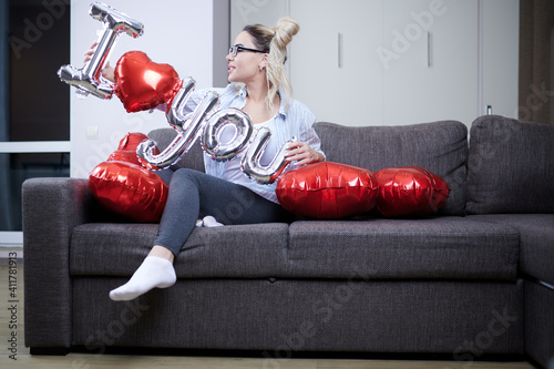 A young beautiful woman is sitting on a sofa and holding exciting balloons