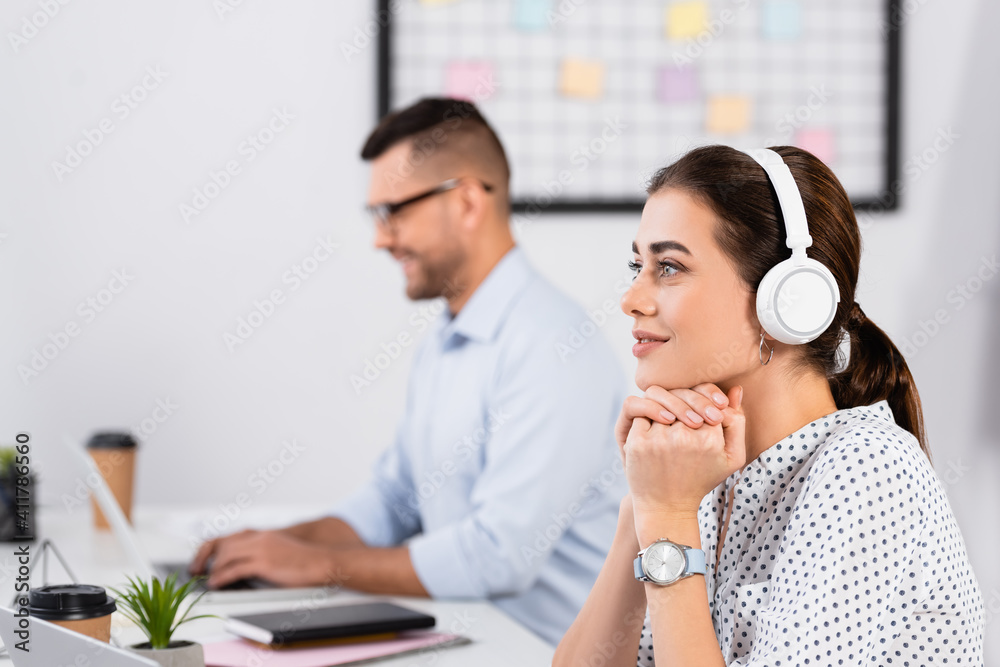 thoughtful businesswoman in wireless headphones near businessman working on blurred foreground thoughtful businesswoman in wireless headphones near businessman working on blurred foreground