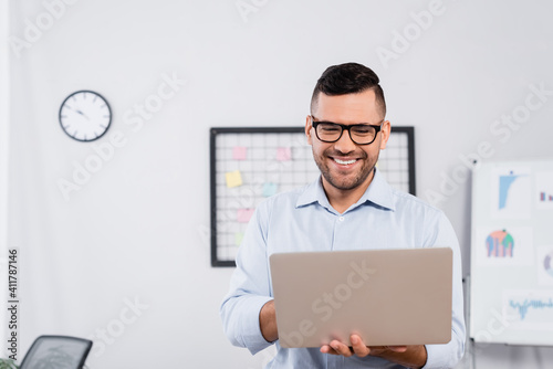 positive businessman in glasses looking at laptop