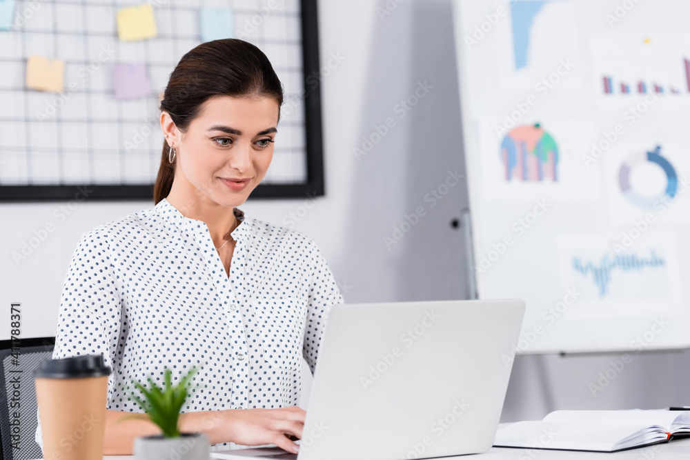 happy businesswoman looking at laptop on desk with blurred foreground happy businesswoman looking at laptop on desk with blurred foreground
