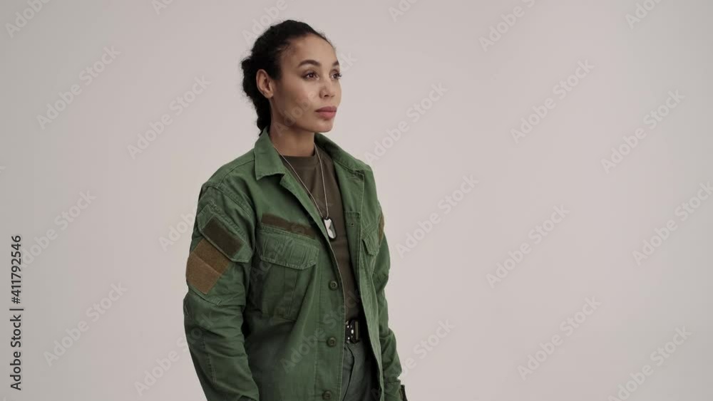 A calm focused young american soldier woman is looking to the side standing isolated over a gray background in the studio A calm focused young american soldier woman is looking to the side standing isolated over a gray background in the studio