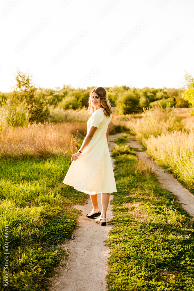 A young beautiful girl with blond curly hair in a light summer yellow dress and with a straw hat in her hands in a field in the countryside at sunset. People and nature A young beautiful girl with blond curly hair in a light summer yellow dress and with a straw hat in her hands in a field in the countryside at sunset. People and nature