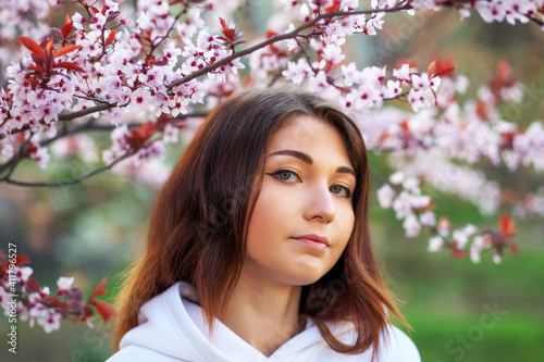 Smiling beautiful girl standing near a peach tree during sunset. Happy face. Spring time.