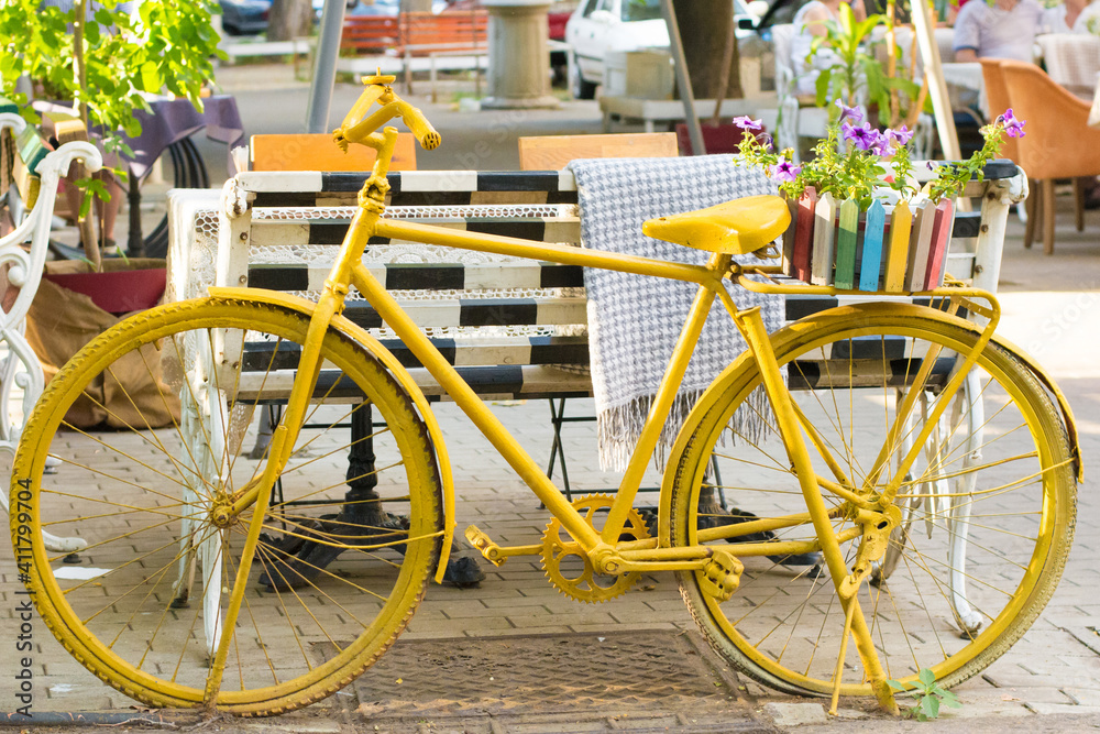 yellow bike on the street with paving stones in sunny weather with flowers