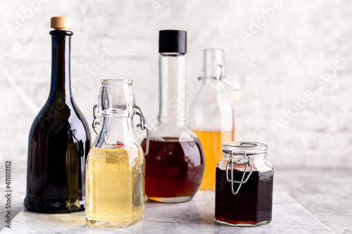 Original glass bottles with different vinegar on a marble table against a background of a white brick wall. Copy space. photo