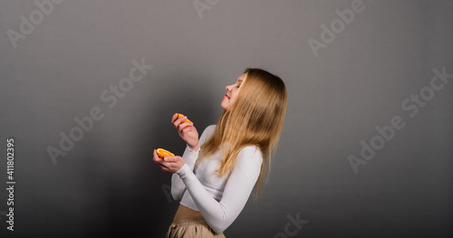 Smiling woman eating orange, half fruit, long hair.