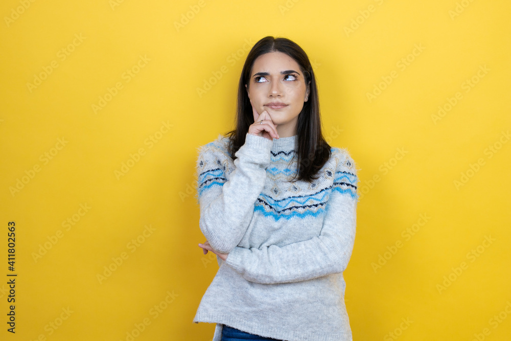 Young caucasian woman wearing casual sweater over yellow background serious face thinking about question with hand on chin, thoughtful about confusing idea Young caucasian woman wearing casual sweater over yellow background serious face thinking about question with hand on chin, thoughtful about confusing idea