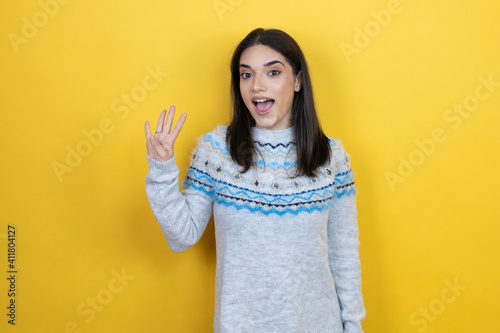 Young caucasian woman wearing casual sweater over yellow background showing and pointing up with fingers number four while smiling confident and happy © Irene