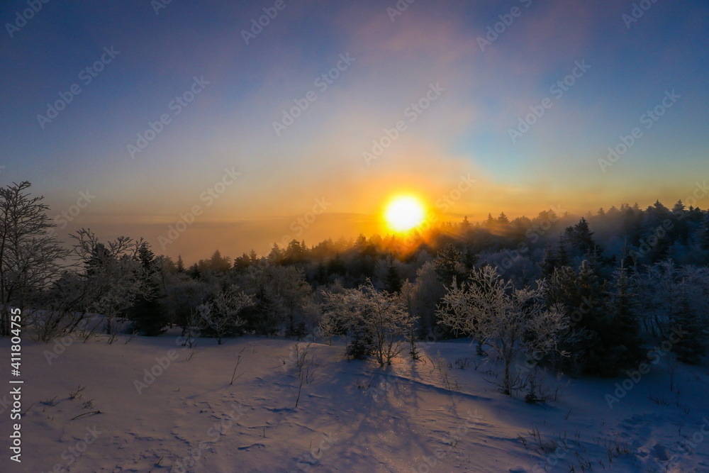 Beautiful winter landscape. The sun sets below the horizon against the backdrop of powdered winter trees atop a snowy mountain. Beautiful winter landscape. The sun sets below the horizon against the backdrop of powdered winter trees atop a snowy mountain.