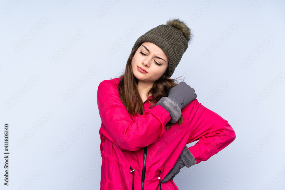 Young girl with winter hat isolated on blue background suffering from pain in shoulder for having made an effort