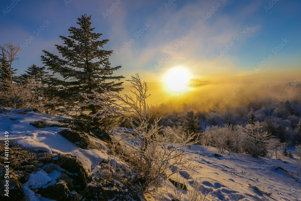 Beautiful winter landscape. The sun sets below the horizon against the backdrop of powdered winter trees atop a snowy mountain.