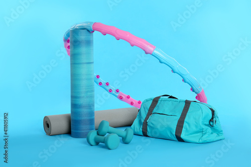 Hula hoop, yoga mats, gym bag and dumbbells on light blue background