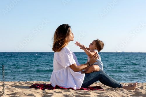 Smiling mom playing with newborn lying on beach towel