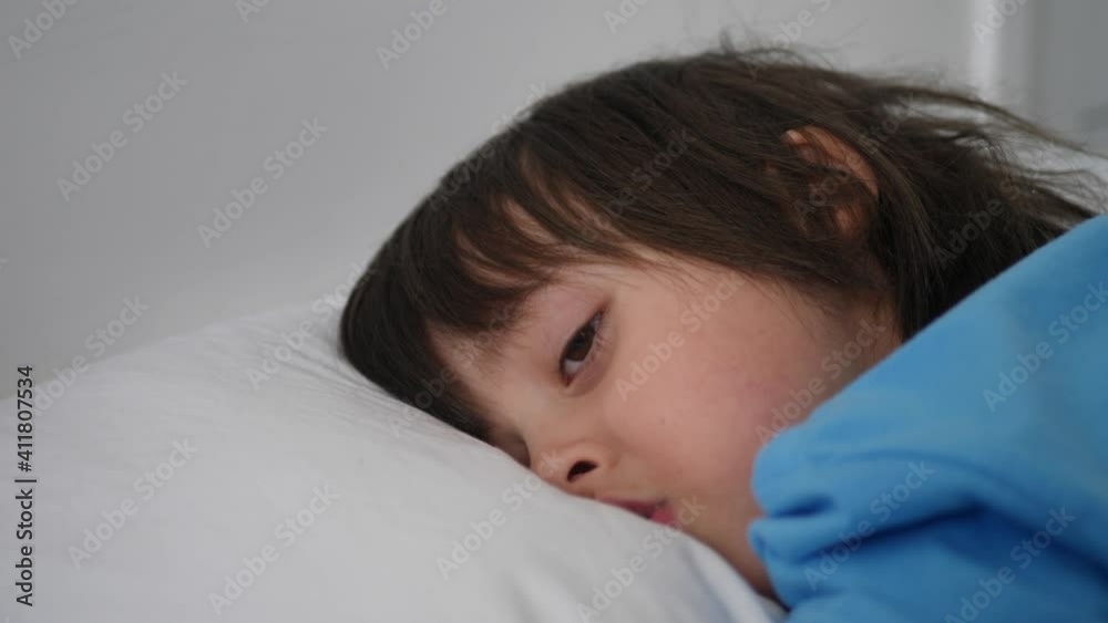 boy child in a blue t-shirt lies on a white bed and falls asleep boy child in a blue t-shirt lies on a white bed and falls asleep