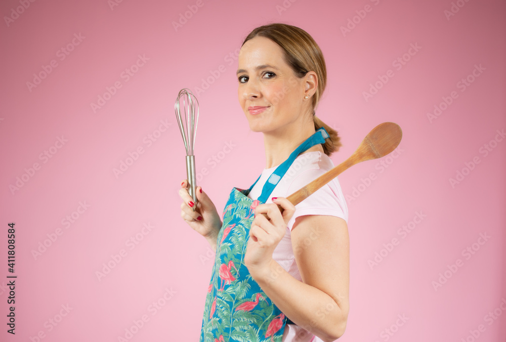 Beautiful young woman holding kitchen utensils over pink background. Beautiful young woman holding kitchen utensils over pink background.
