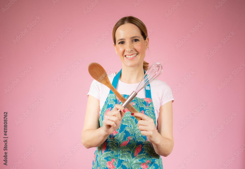 Beautiful young woman holding kitchen utensils over pink background. Beautiful young woman holding kitchen utensils over pink background.