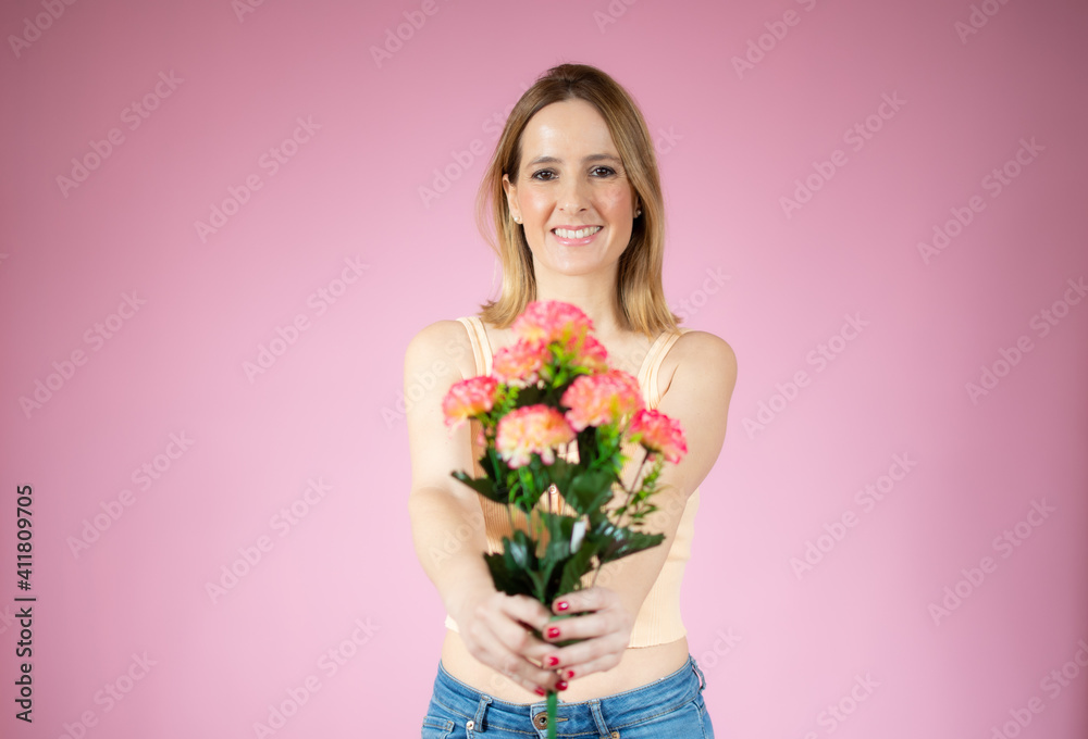 Portrait of a beautiful young woman in casual t-shirt holding big bouquet of flowers isolated over pink background