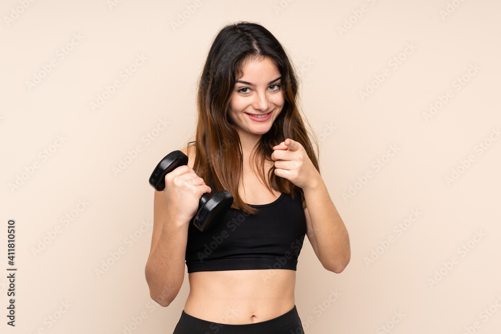 Young sport woman making weightlifting isolated on beige background points finger at you Young sport woman making weightlifting isolated on beige background points finger at you