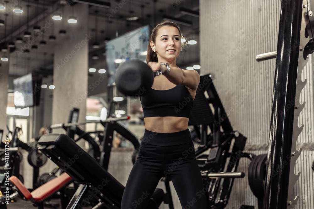 Young athletic woman working out with a kettlebell in her hands, doing swings in the gym Young athletic woman working out with a kettlebell in her hands, doing swings in the gym