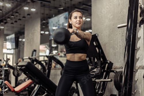 Young athletic woman working out with a kettlebell in her hands, doing swings in the gym