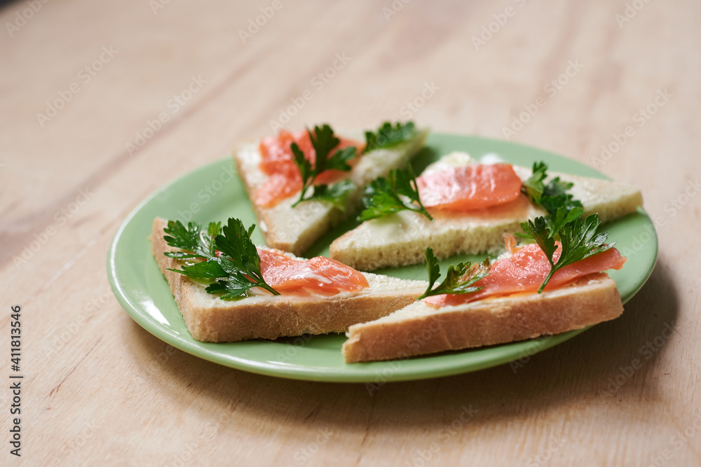 Green plate with salmon sandwiches with butter and parsley on wooden table. Buffet breakfast lunch meal. Healthy eating. Fish diet concept.