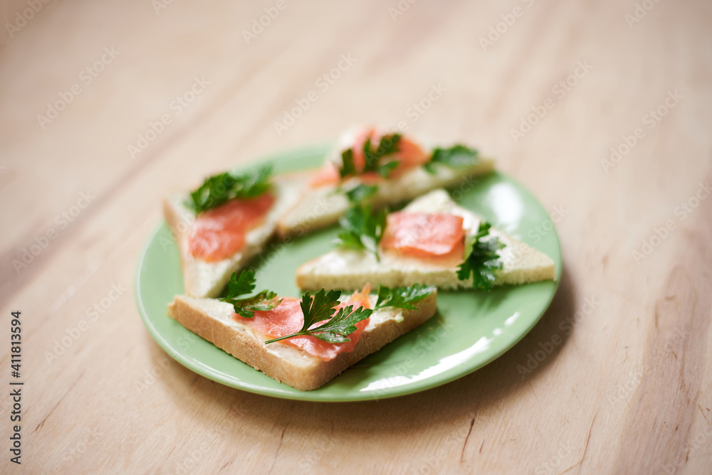 Green plate with salmon sandwiches with butter and parsley on wooden table. Buffet breakfast lunch meal. Healthy eating. Fish diet concept. Green plate with salmon sandwiches with butter and parsley on wooden table. Buffet breakfast lunch meal. Healthy eating. Fish diet concept.