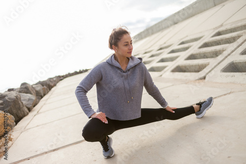 Attractive sporty woman in sportswear trains outdoors. Warm up or stretching leg, healthy lifestyle.