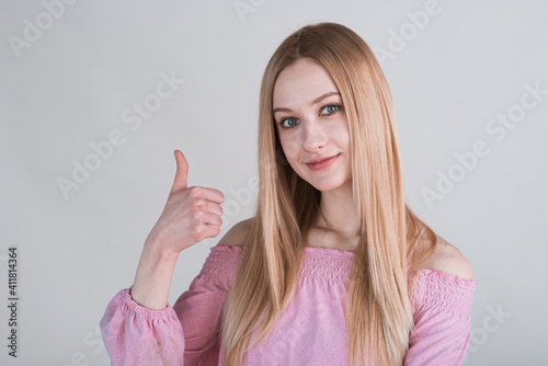 Portrait of a blonde girl who shows thumbs up in the studio on a white background