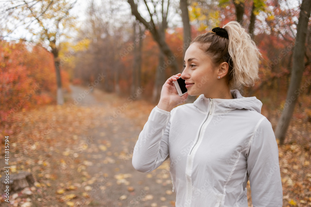 Attractive fitness woman in sportswear talking on the phone in autumn forest Attractive fitness woman in sportswear talking on the phone in autumn forest