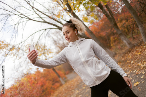 Attractive fitness woman in sportswear makes selfie on smartphone in autumn forest © splitov27