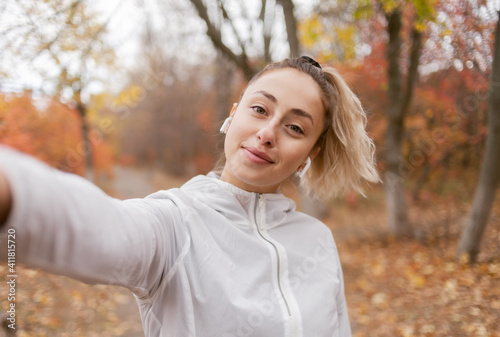 Attractive fitness woman in sportswear makes selfie on smartphone in autumn forest