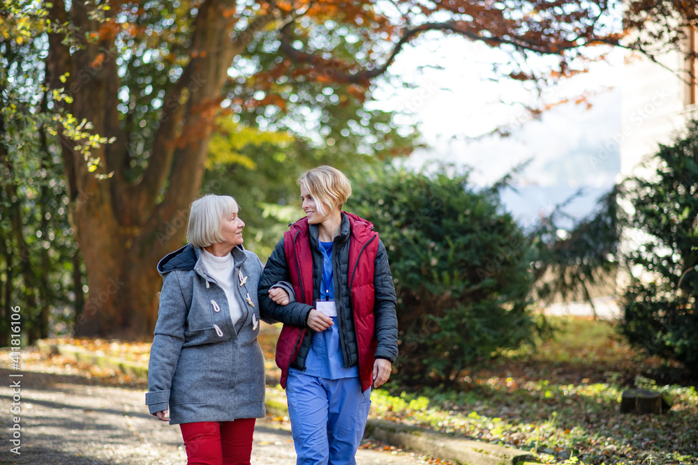 Senior woman and caregiver outdoors on a walk in park, talking.
