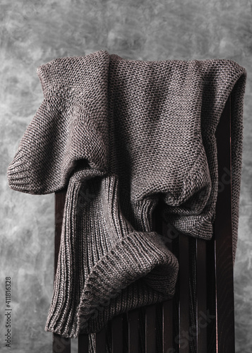 Obraz na płótnie Women's wool knitted gray sweater casually thrown over the back of wooden chair against gray wall. Closeup. Vertical orientation. w salonie